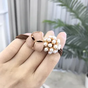 Detail view of pearl and enamel flower hair tie on hand, showing delicate craftsmanship and texture.