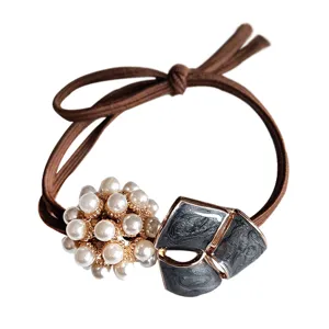 Close-up detail shot of elegant hair tie with pearl cluster and dark grey geometric accent.