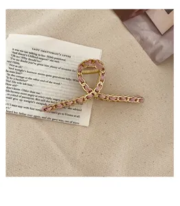Gold metal chain interwoven with pink ribbon hair claw detail, elegant hair accessory for women.