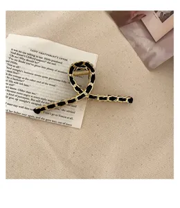 Detail shot of elegant black and gold chain intertwined hair claw clip on textured background.
