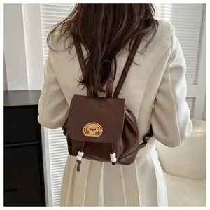Close-up detail shot of a brown mini leather backpack worn by a model, featuring dog patch.