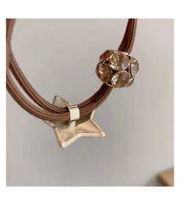 Close-up detail of brown elastic hair tie featuring a sparkling rhinestone ball and star charm.