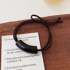 Detailed shot of a minimalist dark brown hair tie with a sleek black curved tube charm.