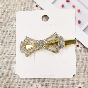 Close-up of a sparkling rhinestone bow hair clip on display card, elegant gold metal hair accessory.