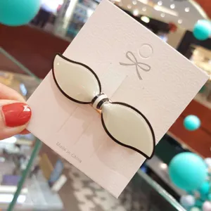 Close-up view of the elegant acrylic bow hair clip on white display card, stylish accessory.