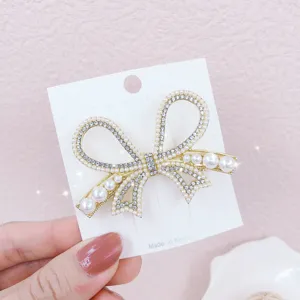 Detail close-up shot of an elegant pearl and rhinestone bow hair clip on display card.