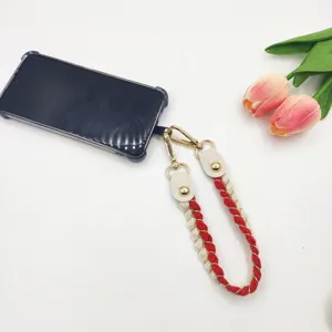 Vue détaillée de la dragonne de téléphone tressée rouge et blanche avec quincaillerie dorée.