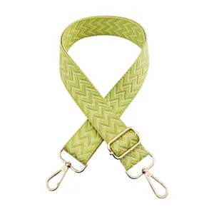 Dettaglio ravvicinato della tracolla larga con motivo chevron verde e fibbie metalliche dorate.