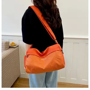Detalle del bolso cruzado a cuadros naranjas que muestra la tela texturizada y correa ancha.