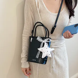 Detail shot of black leather bucket bag with white lace bow and star charm, worn on shoulder.