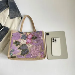 Detail der paillettenbestickten Tasche mit lila Blumenmuster, Strohbesatz und modischem Design.