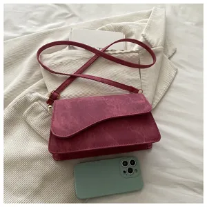 Gedetailleerd overzicht van de elegante magentakleurige suède crossbodytas met klep en gesp.