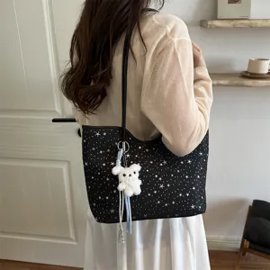 Detailed shot of stylish black starry shoulder tote bag with cute white plush bear pendant.