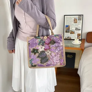 Detailaufnahme der Strohtasche mit lila Pailletten und Blumenstickerei, lässiger Sommerstil.
