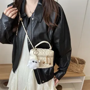 Gros plan sur le sac bandoulière matelassé crème avec chaîne et pendentif fantôme.