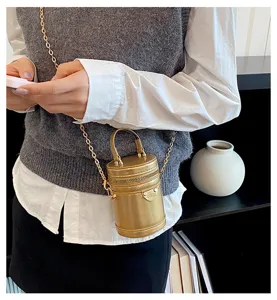 Détail du sac bandoulière cylindrique doré métallique, avec chaîne et poignée pour un style tendance.