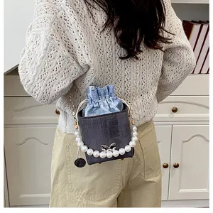 Stylish pearl chain bucket bag detail featuring denim drawstring pouch and metal bow accent.