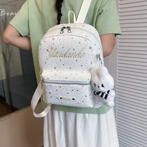 Detailed view of white star print backpack with cute fluffy bunny keychain and front zipper pockets.