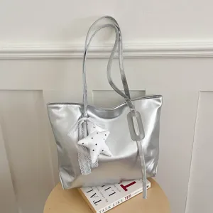 Vue détaillée d'un sac cabas métallisé argenté avec joli pendentif étoile sur table.