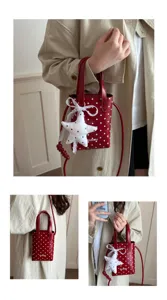 Detalle de bolso bandolera pequeño de lunares rojos con diseño de viajero elegante.