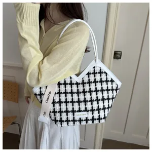Zwart-witte tweed schoudertas met houndstooth motief, V-vormig ontwerp en witte lederen rand.