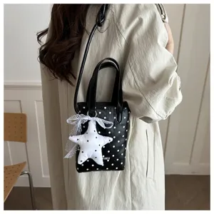 Vista detallada del bolso de lunares negros de moda con colgante de estrella blanca.
