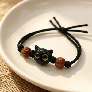 Close-up of a black kitten cord bracelet with two decorative marbled brown beads on a dish.