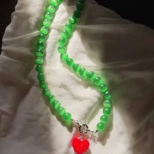 Dettaglio collana di perle occhio di gatto verde con ciondolo a cuore rosso su stoffa.