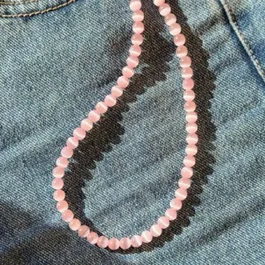 Vista dettagliata della collana di perle occhio di gatto rosa su sfondo denim blu estivo