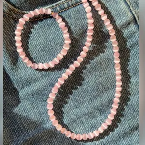 Dettaglio della collana e del bracciale di perle occhio di gatto rosa su jeans