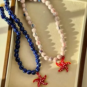 Détail de colliers en perles avec pendentifs étoile de mer rouge dans un plateau.