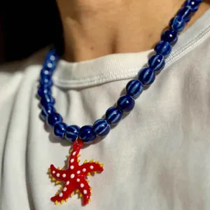 Gros plan d'un collier de perles rayées bleues avec pendentif étoile de mer rouge.