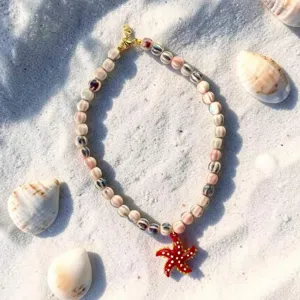 Détail d'un collier de perles avec un pendentif étoile de mer rouge sur sable blanc