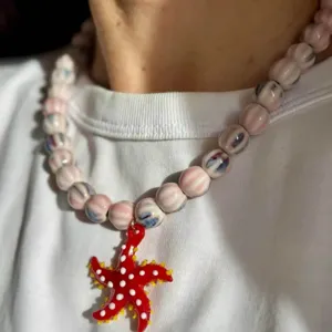 Détail rapproché d'un pendentif étoile de mer rouge vif sur un collier en perles de verre.