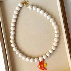 Vue détaillée d'un collier en perles de lave blanche avec un pendentif poisson en verre orange