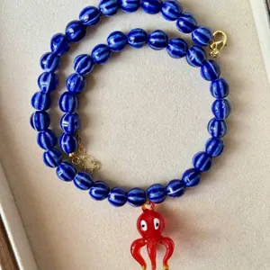 Vue détaillée d'un collier de perles à rayures bleues avec pendentif poulpe rouge