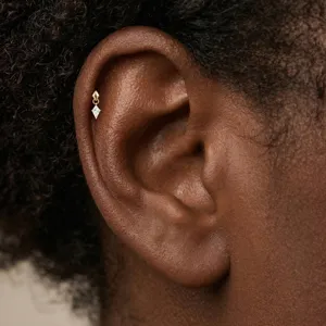Detailed macro view of a kite-cut diamond helix piercing worn on a dark-skinned ear