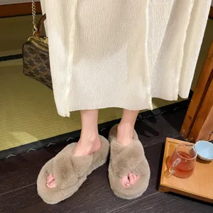 Close-up shot of beige fuzzy cross-strap slippers worn by a model in a cozy home setting