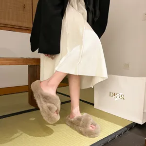 Detail view of khaki fuzzy cross-strap slippers worn in a cozy indoor setting