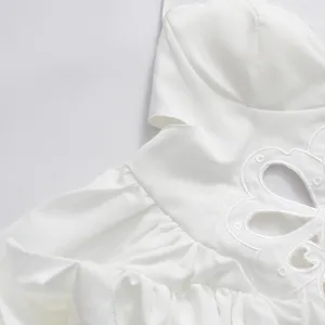 Close-up view of a white dress with embroidered floral cut-out and ruffles