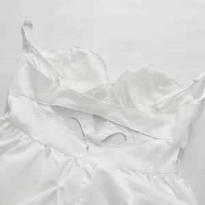 Close-up of white strap dress featuring back hollowed-out floral carving and zipper detail.