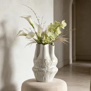 Primo piano di un vaso in ceramica bianca Wabi-sabi con trama ondulata e fiori