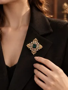 Detailaufnahme einer Vintage-Brosche mit Smaragdkristall auf einem schwarzen Blazer.