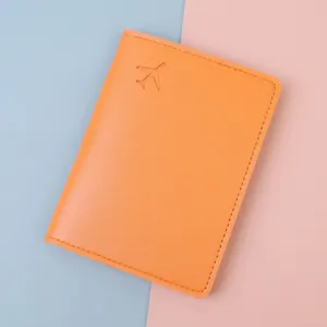 Nahaufnahme der orangefarbenen Reisepasshülle mit Flugzeug-Prägung und Ledertextur.