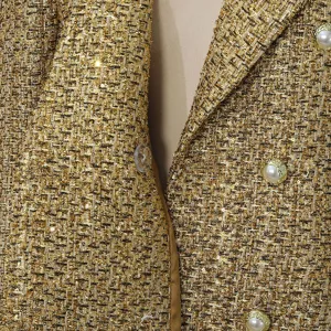 Close-up detail of golden tweed fabric with elegant pearl buttons on women's coat