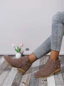 Close-up detail of side zipper and buckle on stylish brown pointed-toe ankle boots.