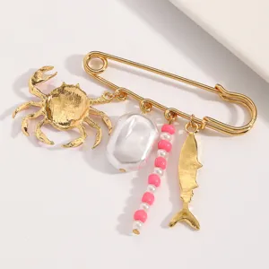 Dettaglio di una spilla dorata con ciondoli a forma di granchio e perla stile marino.