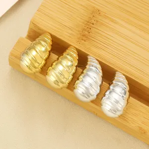 Detailansicht von gold- und silberfarbenen CCB-Ohrringen in Schneckenform auf Holz