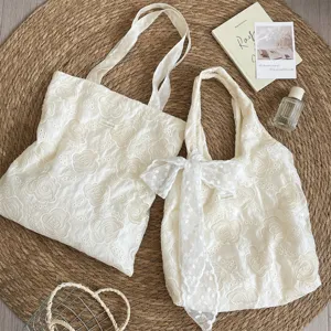 Détail de sacs cabas français brodés ajourés blanc cassé sur un tapis de paille