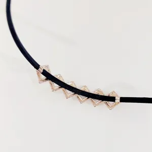 Close-up detail van zwarte leren koord ketting met geometrische ruitvormige metalen hangers.